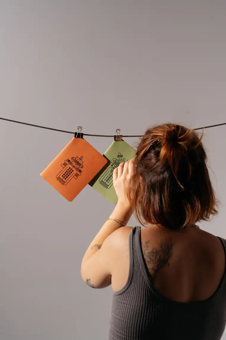 Hanging an orange and a green notebook on the line before a frame.