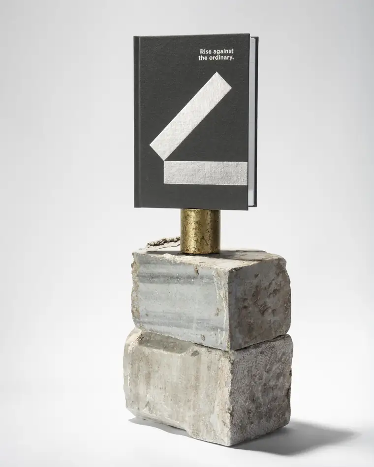 A charcoal notebook reading Rise against the ordinary on stacked concrete blocks.