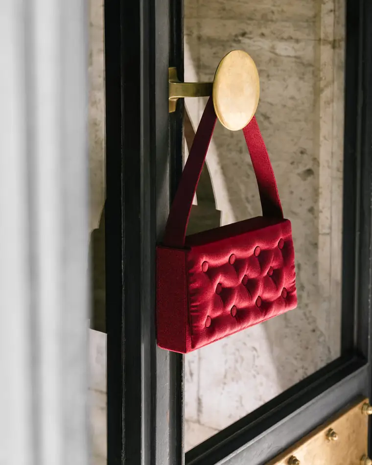 Burgundy bag hanging from a brass hook on a mirrored door.