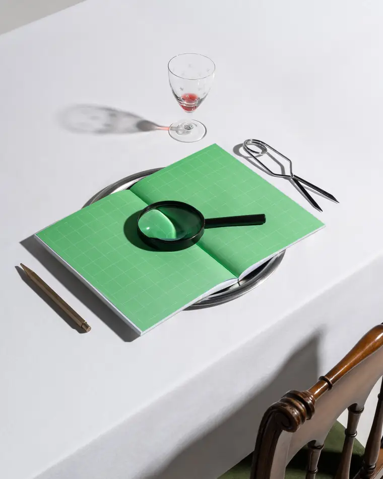 A green grid notebook opened on a plate under a magnifying glass.