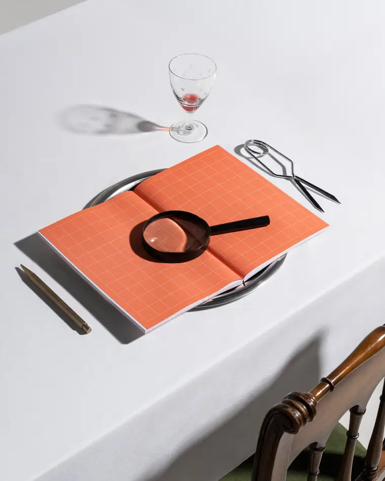 An orange grid notebook opened on a plate under a magnifying glass.